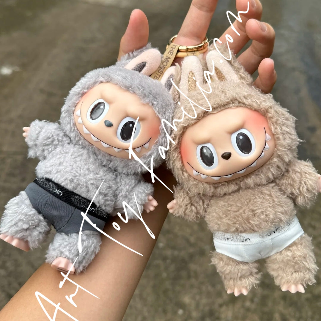 POP MART Two plush the monsters labubu keychains with cute underwear outift held by a hand against a blurred background